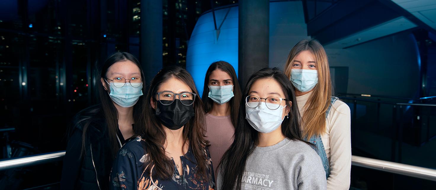 Pharmacy Students for Antimicrobial Stewardship Society members standing in front of pods in Leslie Dan Faculty of Pharmacy building lit up blue