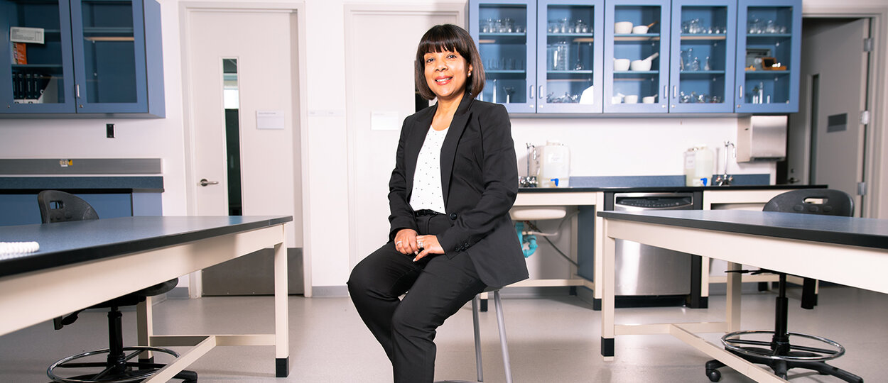 Portrait of Lachmi Singh sitting in front of blue pharmacy shelves