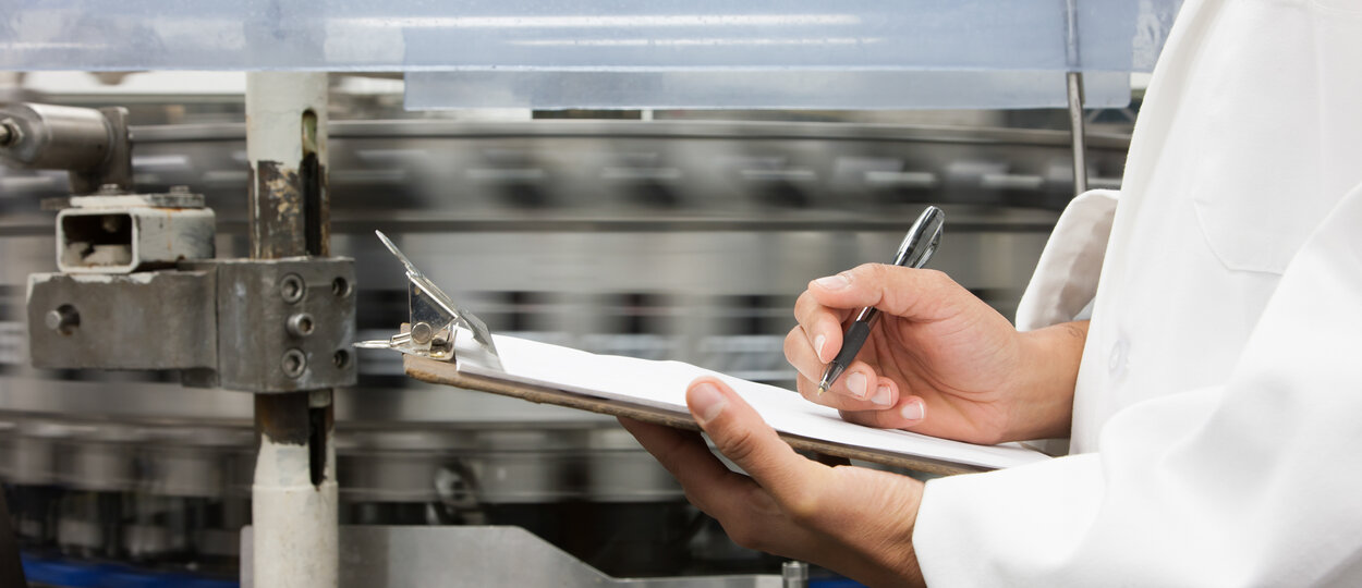 Focused hands writing on clipboard with factory background