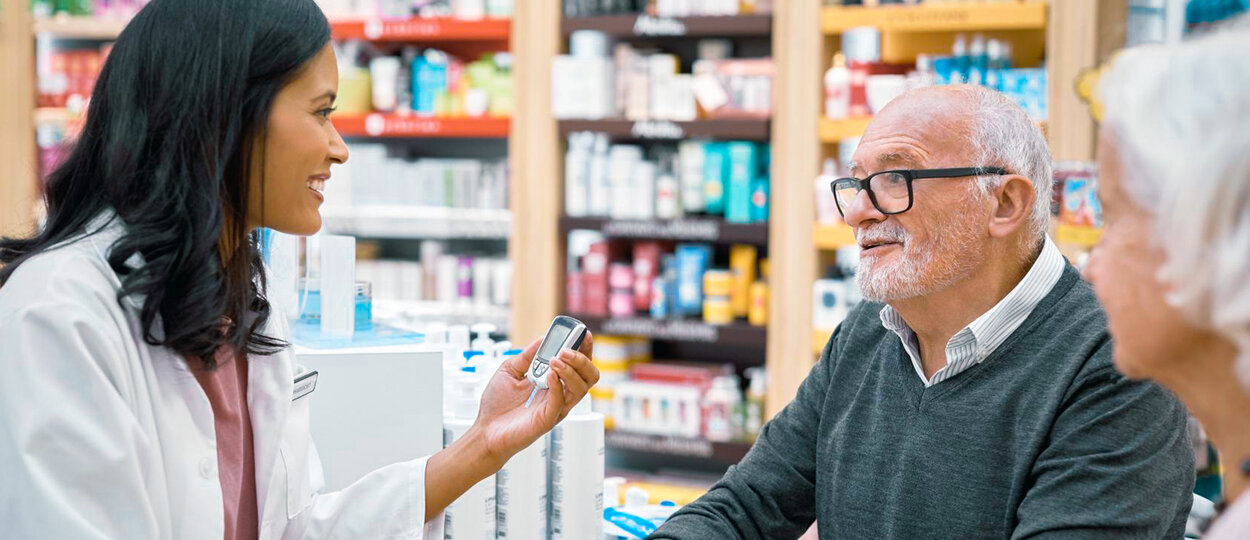 elderly man being counselled by young female pharmacist on use of glucose monitor