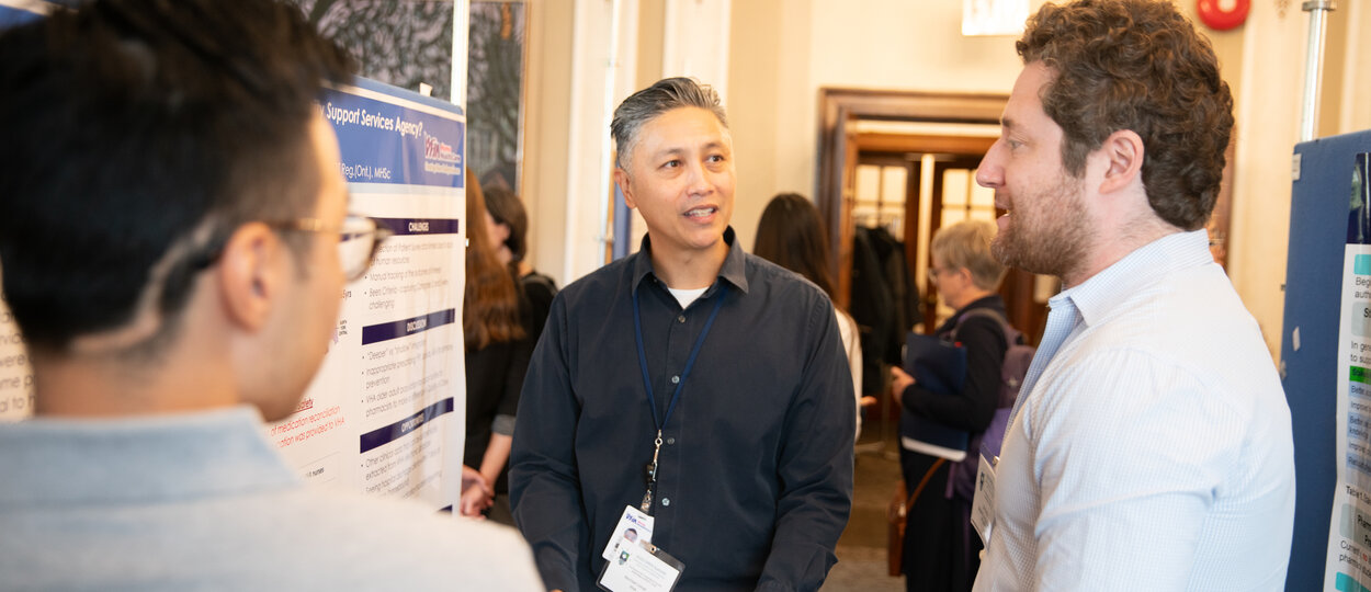 Attendees and presenters at 2023 OPEN Symposium having a discussion in front of research poster