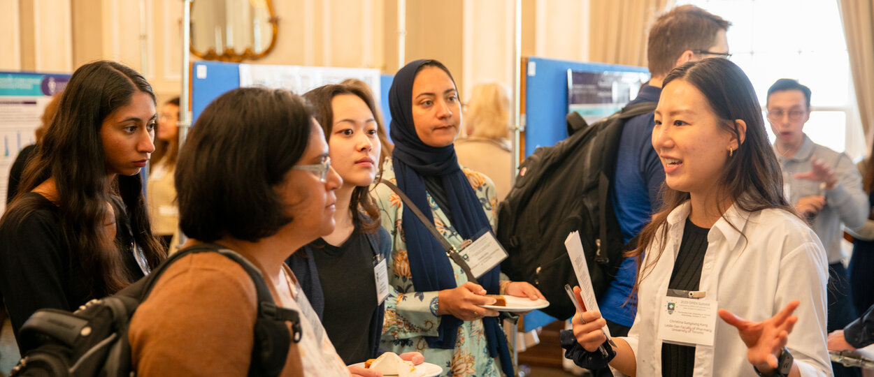 Attendees and presenters at 2023 OPEN Symposium having a discussion in front of research poster