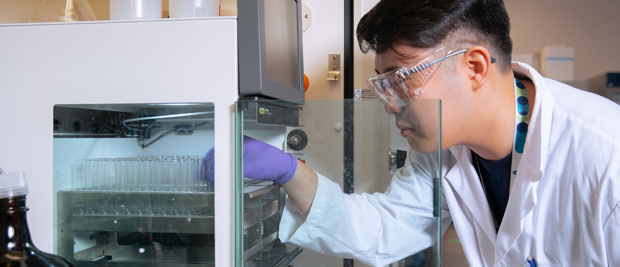 Image of PhD trainee Jingan Chen placing speciman tubes in machine