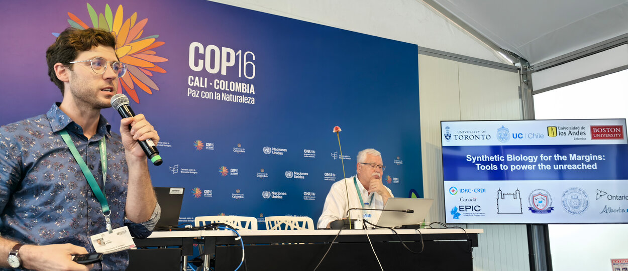 Scientist speaking in front of crowd with presentation screen behind them