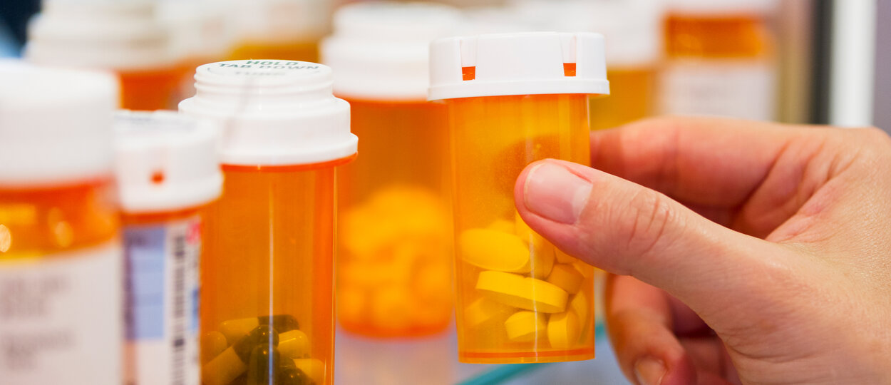 Hand grabbing generic pill bottles on shelf