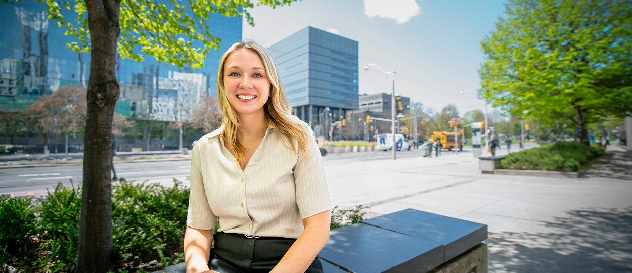 Jenna Sauvé sitting across the street from the Leslie Dan Faculty of Pharmacy building