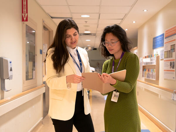 Two pharmacists reviewing a patient file in a hospital hallway