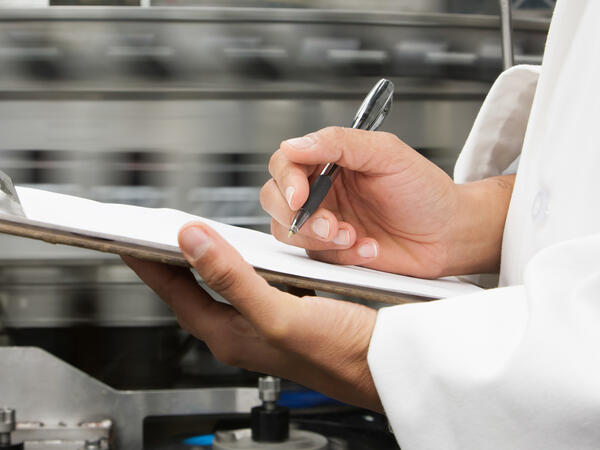 Focused hands writing on clipboard with factory background