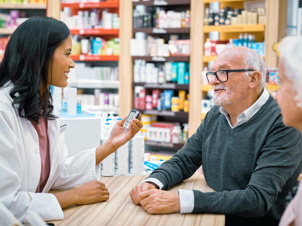 elderly man being counselled by young female pharmacist on use of glucose monitor