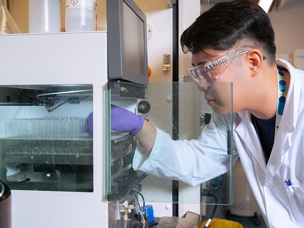 Image of PhD trainee Jingan Chen placing speciman tubes in machine