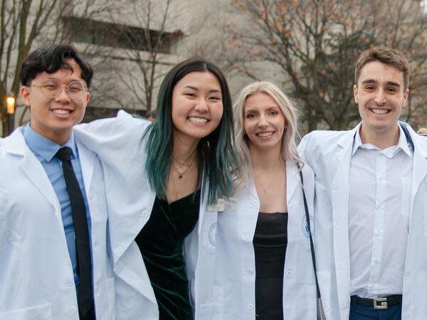 Two female and two male-presenting students wearing white lab coats with circular Pharmacy crest