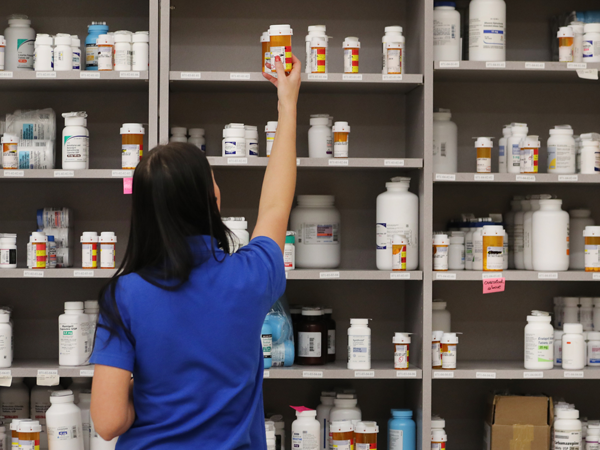 A pharmacy technician grabs a bottle of drugs off a shelf