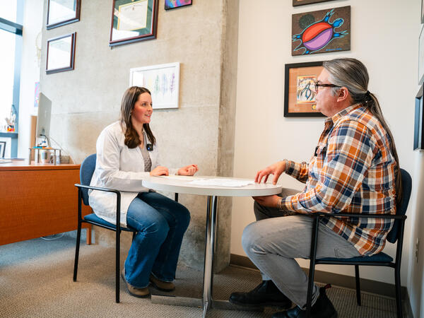 Third Year PharmD student Cloé Lafleur conducts medication management consultation with patient actor Brandon Oakes Pharmacy Student and Indigenous patient sitting at table talking