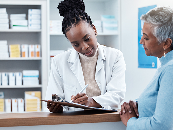 Pharmacist and patient reviewing paper work at pharmacy counter Pharmacist and patient reviewing paper work at pharmacy counter
