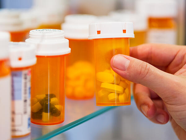Hand grabbing generic pill bottles on shelf