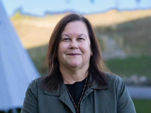 Portrait of woman standing outdoors with grassy hill and blue sky in background
