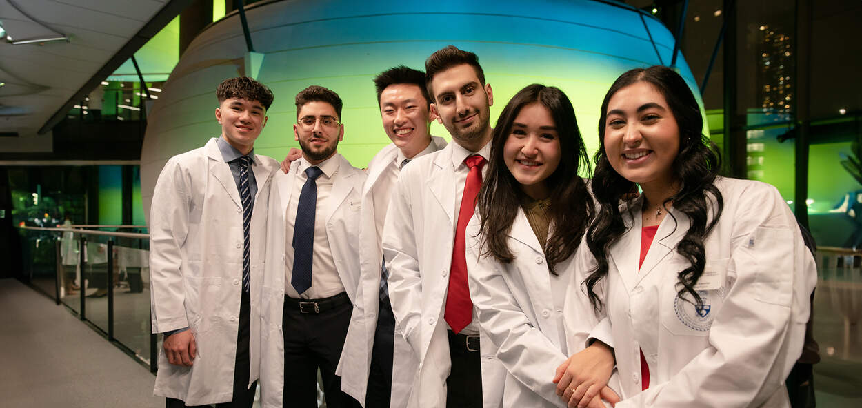 Six PharmD students in white coats in front of 2nd floor Pod in Leslie Dan Faculty of Pharmacy